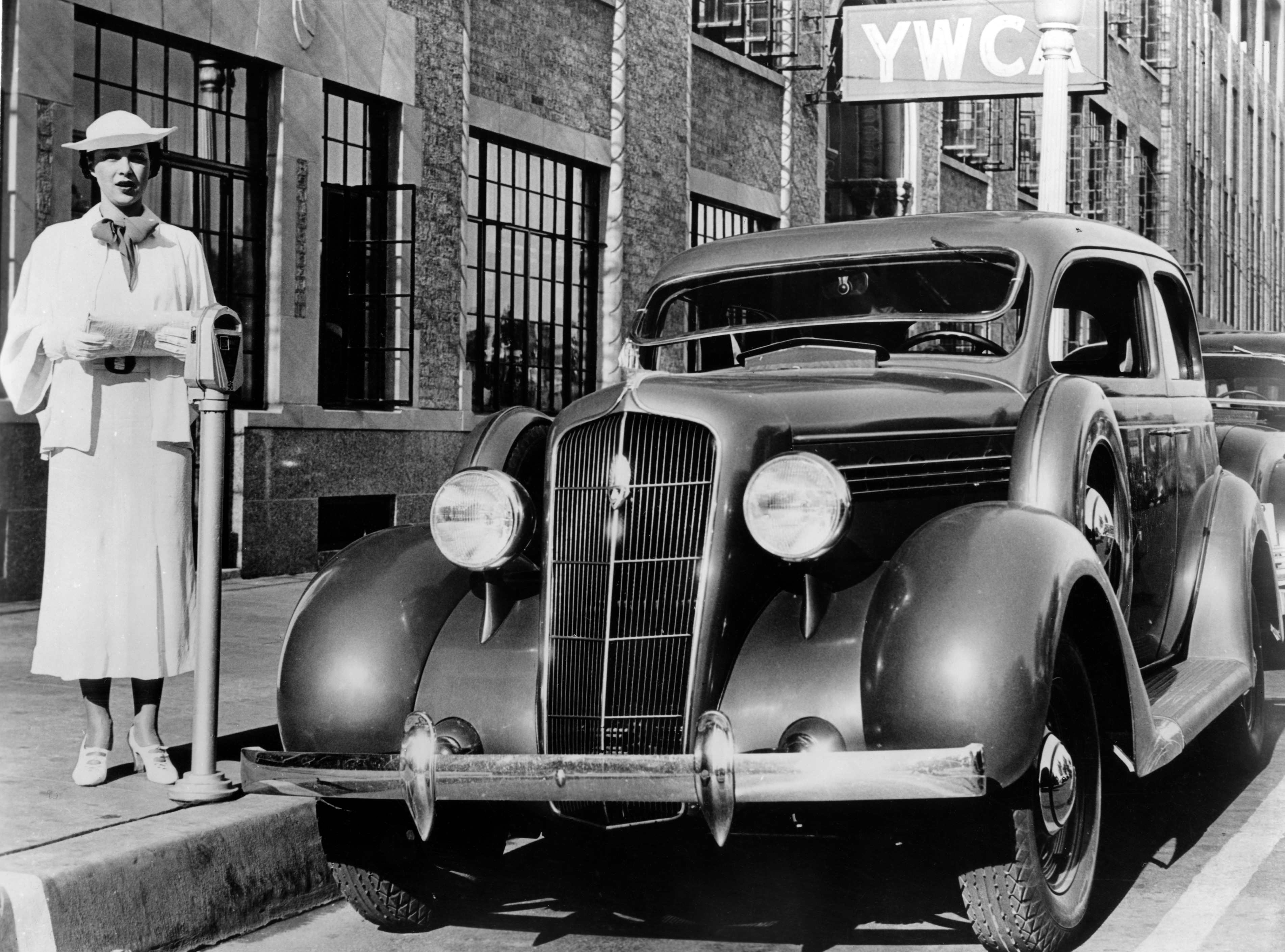 Black and white photograph of a woman paying for parking at a parking meter.