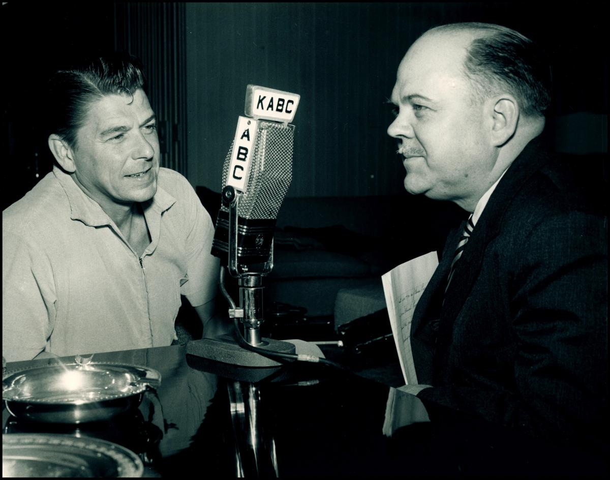 Ronald Reagan sits in front of a microphone with reporter Ted Malone.