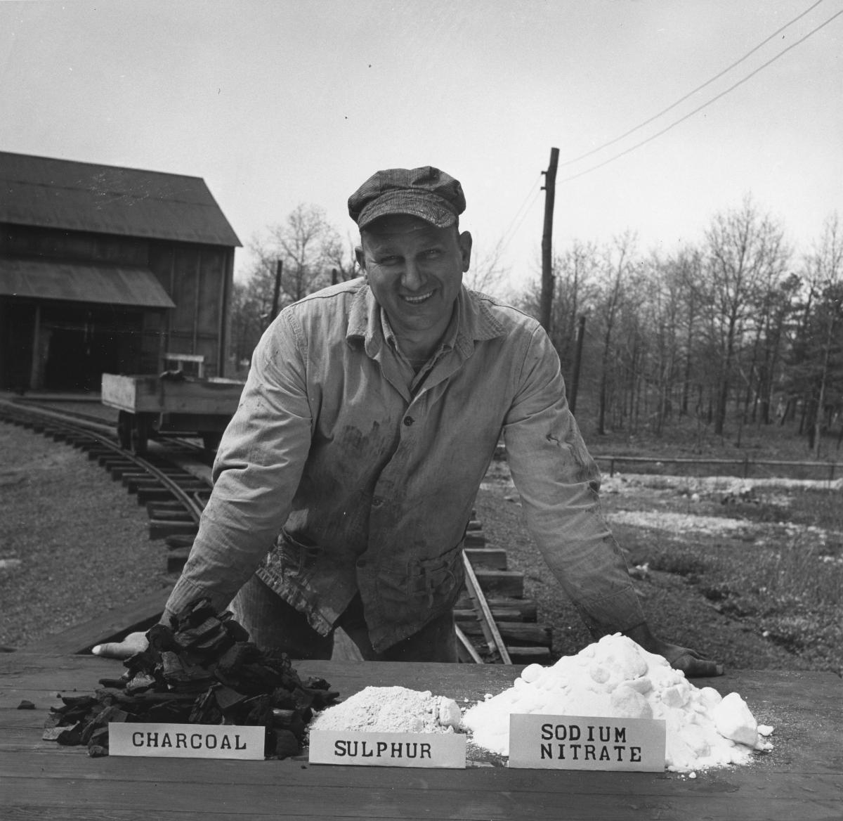 A man stands in front of piles of the three ingredients comprising of black powder.