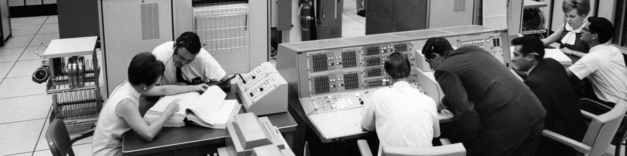 People use large scale computers in this 1960's era photo.