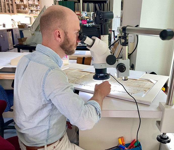 Luke Kelly using a microscope while conserving Penn land documents