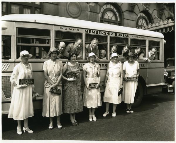 Photograph of women from the Women's Organization for National Prohibition Reform, posed with signs in front of a bus with men looking out the window