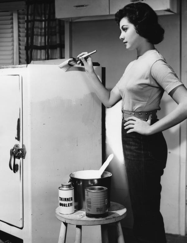 Black and white image of a woman painting a refrigerator