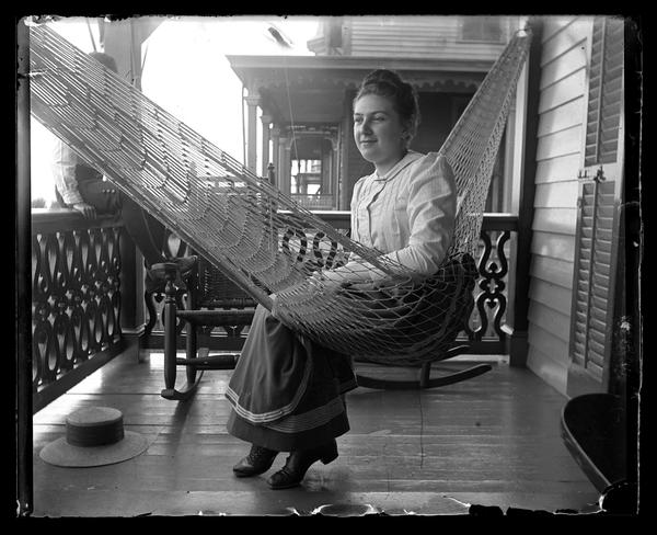 Black and white photograph of a woman in a hammock on a porch