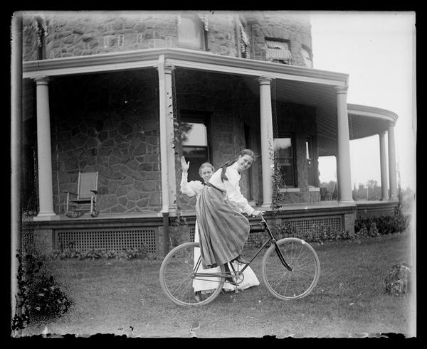 Two women on a lawn with a bicycle in front of St. Amour, a du Pont family home.