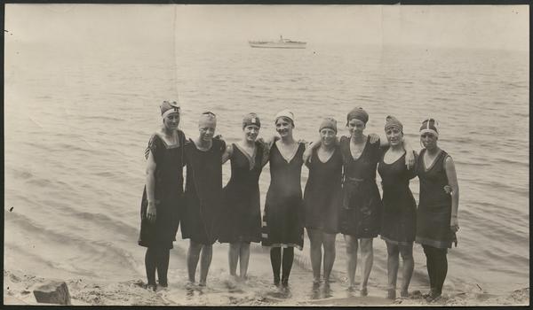 Black and white photograph of a group of women posed by the shore of a beach in 1916
