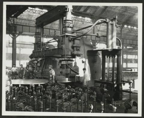 Black and white photograph from inside a Bethlehem Steel factory, showing workers and large industrial shearing equipment.