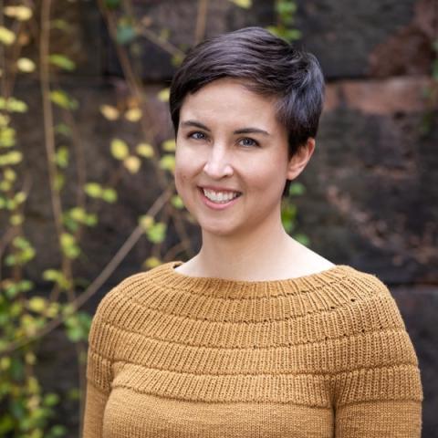 Charlotte Leib, a woman with short dark brown hair and wearing a yellow sweater smiles at the camera.