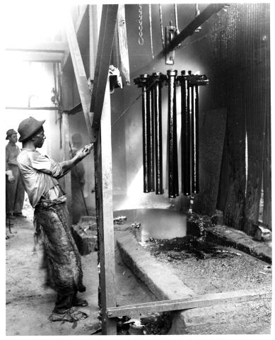 Black and white photograph of a worker coating cast iron pipes with bitumen (Birmingham, Ala.)