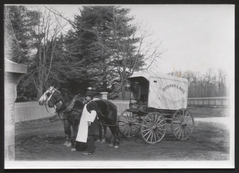 A man in an apron stands by a horse-drawn delivery wagon labeled "RAYNOR & BRO." 