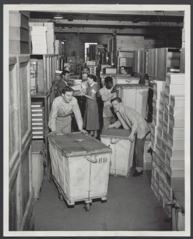 People working in a corridor of a storage room or warehouse of a Strawbridge & Clothier store.