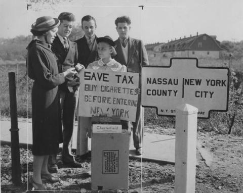 People buying and selling cigarettes by a sign demarcating the Nassau and New York City county line