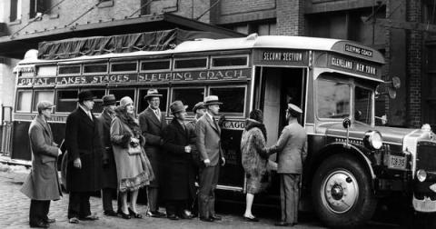 A black and white photograph of a group of people boarding a bus.