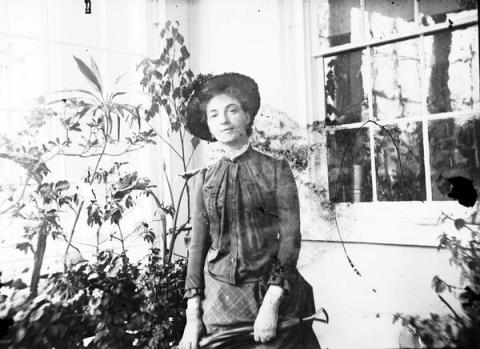 Black and white image of a woman holding a shovel in a greenhouse conservatory