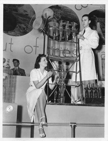 BBlack and white image of a man and woman at an exhibition showcasing a complex apparatus.