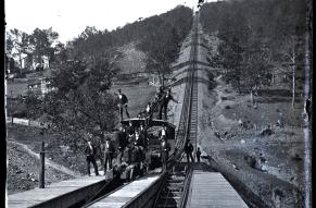 lack and white a image of a railcar at the base of a steep incline, with people aboard and nearby.