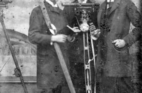 Black and white tintype photograph of three young men posed with surveying equipment.