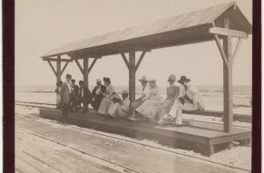 Black and white photograph of a group of people assembled at a seaside streetcar station.