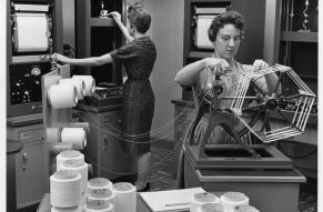 Black and white photograph of two women in a laboratory testing strands of Lycra fiber.