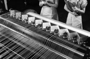 Black and white image of two women overseeing the manufacture of synthetic fibers on a machine.