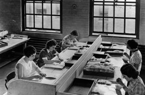 Black and white photograph of women in a factory picking out black and yellow bristles from the washed white stock.