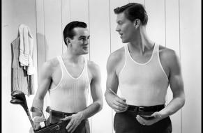 Black and white image of two men in undershirts with a golf bag.