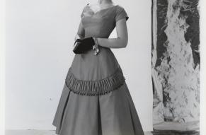 Black and white photograph of a woman in a calf-length cocktail dress, with a red fabric sample