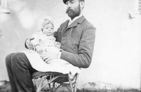 Black and white image of a man in a rocking chair with an infant in his lap
