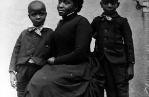 Posed portrait of a seated woman and two standing children, dressed in late 19th-century clothing.