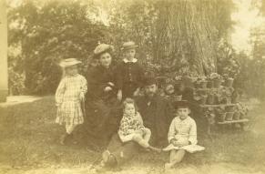 Sepia-tinged photograph of a family with small children, posed in a yard by a container garden