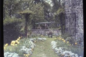 Autochrome image of a garden in bloom with a stone building and garden swing