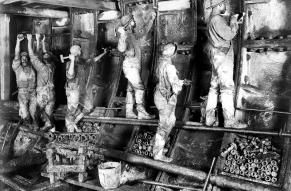 Black and white image of workers hammering and tightening construction elements along the wall of an underground railroad tunnel.