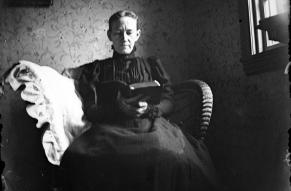Black and white glass negative image of a seated woman reading a book.