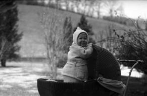 Black and white image of a baby bundled in warm clothing standing in his carriage