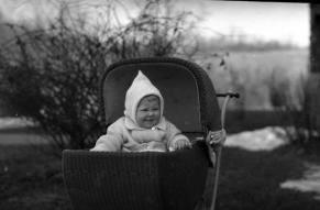 Black and white photograph of a baby, warmly dressed, in a baby carriage.