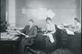 Black and white oimage of a man and two women working in an office, ca. 1910.