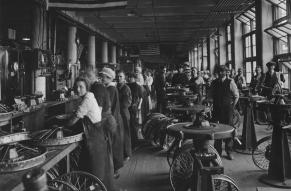 Black and white image of workers on assembly line in wheel factory