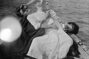 Glass negative image of two women in a rowboat, draped dramatically on top of one another.