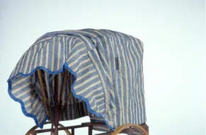 A small, two-wheeled carriage made of wood with a blue and white striped canopy.