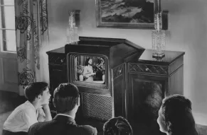 Black and white photo of a mid 20th century family gathered around a TV set