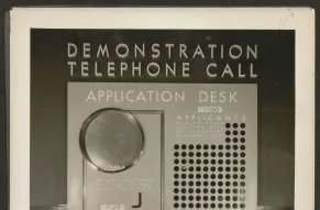 Black and white image of three women at a demonstration telephone call application desk.