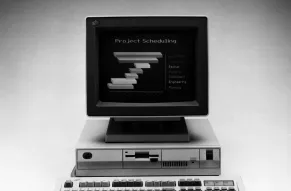 A black and white photograph of a vintage desktop computer. It has CRT monitor displaying several lines of text.