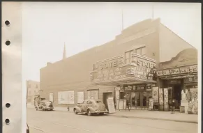 Black and white photograph of a 1930s movie theatre on a commercial street.