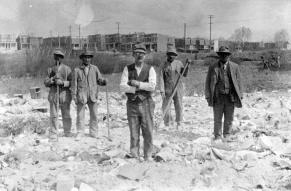 Black and white image of workmen on a cleared construction site.