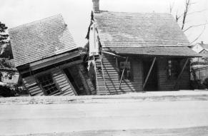 Black and white image of a house split vertically by flooding.
