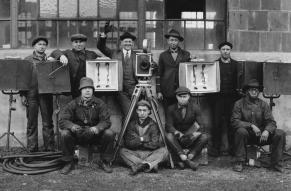 Black and white group photograph of nine men with motion picture equipment and cameras.