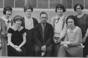 Black and white posed group portrait of six woman and a man in 1920s clothing.