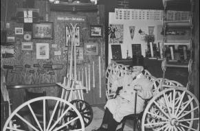 Black and white image of a man in a coat and top hat, seated in a booth exhibiting the works of the Hoopes Brothers & Darlington company. 