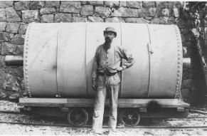 Black and white image of a bearded person standing in front of an industrial glazing barrel.