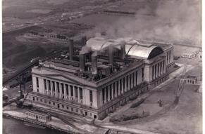 Black and white aerial photograph of a large electric plant located along a river.